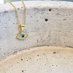 May include: A gold chain necklace with a blue and white evil eye pendant. The pendant is oval shaped and has a gold rim.