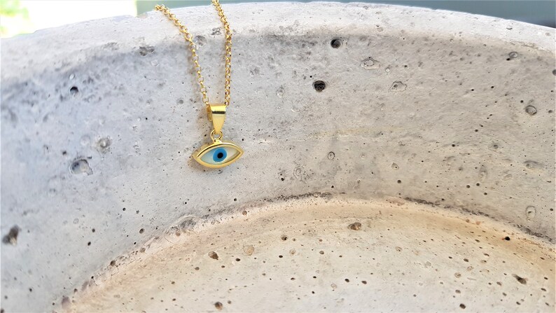 May include: A gold chain necklace with a blue and white evil eye pendant. The pendant is oval shaped and has a gold rim.