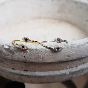 May include: Two gold and silver rings with blue evil eye charms. The rings are on a white background.