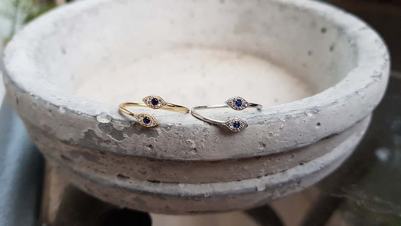 May include: Two gold and silver rings with blue evil eye charms. The rings are on a white background.
