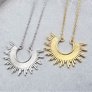 May include: Two delicate necklaces with sunburst pendants. One necklace has a silver pendant and the other has a gold pendant.