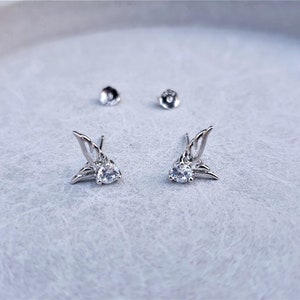 May include: A pair of silver earrings with a clear crystal in the center of each earring. The earrings are shaped like wings.