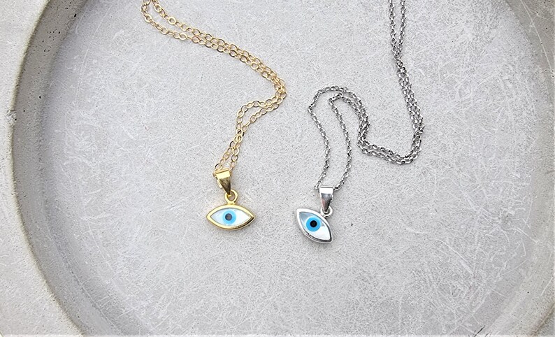 May include: Two silver necklaces with blue evil eye pendants. One necklace is gold and the other is silver.