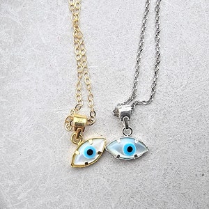 May include: Two necklaces with evil eye pendants. One necklace has a gold chain and the other has a silver chain. Both pendants are white with a blue eye.