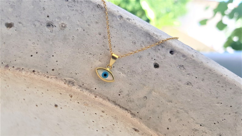 May include: A gold chain necklace with a blue and white evil eye pendant. The pendant is a small, oval-shaped charm with a blue eye in the center.
