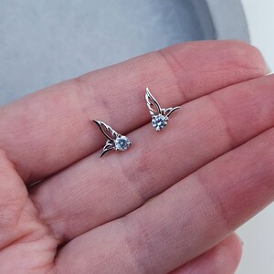 May include: A pair of silver earrings with small, clear crystal stones and delicate wing designs.