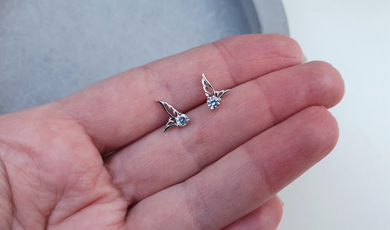 May include: A pair of silver earrings with small, clear crystal stones and delicate wing designs.