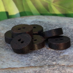 Puede incluir: Un montón de botones de madera marrón oscuro con dos agujeros cada uno. Los botones están dispuestos en un patrón aleatorio sobre una superficie de piedra gris.