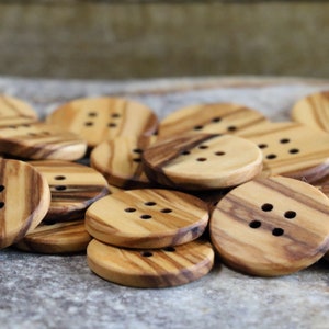 May include: A pile of wooden buttons with four holes each. The buttons are made of light brown wood with dark brown stripes.