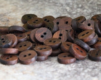 May include: A pile of brown wooden buttons with two holes each. The buttons are arranged in a random pattern on a light brown surface.