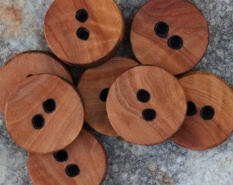 Puede incluir: Un conjunto de ocho botones de madera, cada uno con dos agujeros negros. Los botones son de color marrón claro y tienen una veta de madera natural.