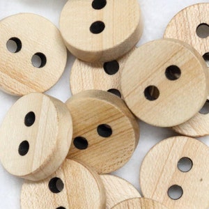 Puede incluir: Un grupo de diez botones de madera, cada uno con dos agujeros. Los botones son de color marrón claro y tienen un acabado liso y natural.