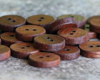 May include: A pile of brown wooden buttons with two holes each. The buttons are arranged in a random pattern on a grey stone surface.
