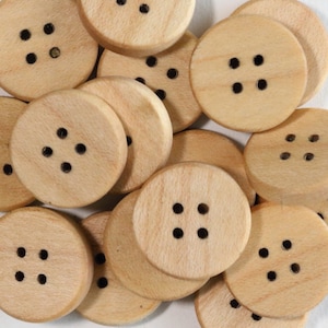 Puede incluir: Un montón de botones de madera, cada uno con cuatro agujeros. Los botones son de color marrón claro y tienen un acabado liso.