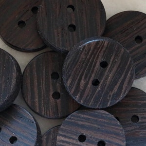 May include: A group of ten dark brown wooden buttons with two holes each. The buttons have a wood grain pattern.