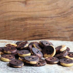 Op de afbeelding: Een stapel bruine en gele houten knopen met elk twee gaten.