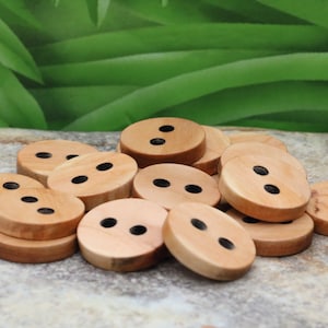 Puede incluir: Un montón de botones de madera con dos agujeros cada uno. Los botones son de color marrón claro y tienen un acabado liso y pulido.