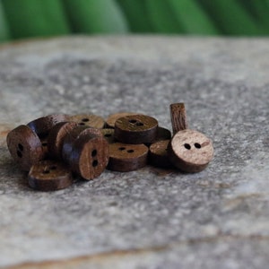 May include: A pile of brown wooden buttons with two holes each. The buttons are arranged in a random pattern on a gray surface.