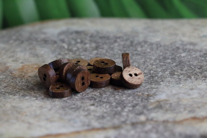 May include: A pile of brown wooden buttons with two holes each. The buttons are arranged in a random pattern on a gray surface.