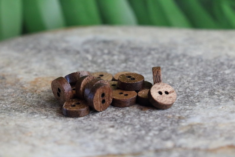 May include: A pile of brown wooden buttons with two holes each. The buttons are arranged in a random pattern on a gray textured surface.