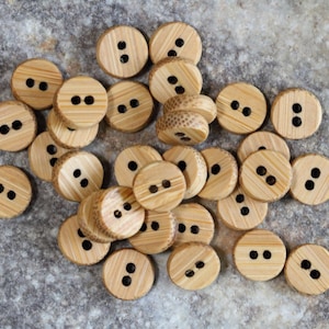 May include: A collection of natural wood buttons with two holes each. The buttons are round and have a light brown colour.