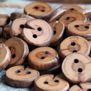 Op de afbeelding: Een close-up van een stapel houten knopen met elk twee gaten. De knopen zijn lichtbruin van kleur en hebben een natuurlijke houtnerf.