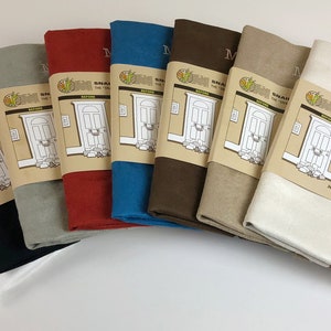 May include: A set of eight door draft stoppers in various colors, including white, black, gray, red, blue, brown, beige, and cream. The stoppers are made of fabric and have a simple design with the words "Draft Saver" and "The Door That Catches for Mini Drafts" printed on the label.