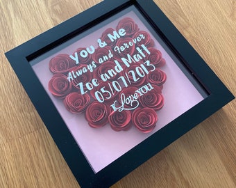 May include: A black framed shadow box with a pink background and a heart made of red paper roses. The text "You & Me Always and Forever Zoe and Matt 05/07/2013 I Love You" is written in white on the glass.