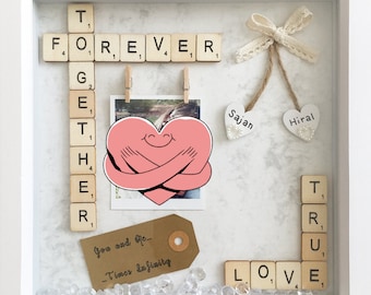 May include: A white picture frame with a white background and a heart with arms hugging itself. The frame contains a photo, a tag that says "You and Me... Times Infinity", and Scrabble tiles spelling out "FOREVER TOGETHER TRUE LOVE".