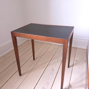 May include: A rectangular side table featuring a dark brown wooden frame with four straight, tapered legs and a smooth, matte black tabletop surface. The table has a clean, simple construction with visible wood grain on the frame.