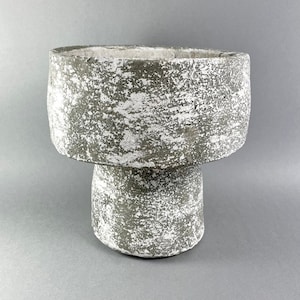 Könnte beinhalten: Ein grauer Keramiktopf mit einer abgenutzten weißen Oberfläche. Der Topf hat eine breite, runde Oberseite und einen Sockel.