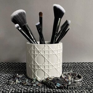 Maceta de color blanco roto, hecha a mano en estilo minimalista con un patrón gráfico, soporte para pinceles o bolígrafos.