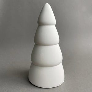 Puede incluir: Un adorno de &aacute;rbol de Navidad de cer&aacute;mica blanca con un dise&ntilde;o escalonado. El adorno es liso y tiene una forma redondeada.