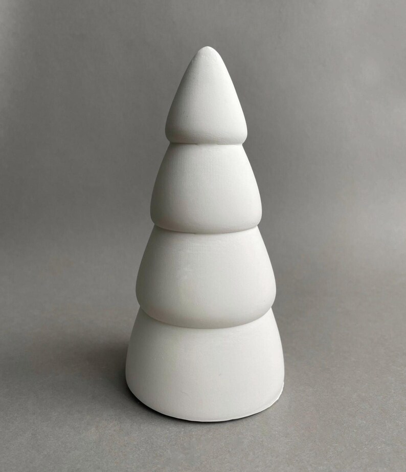 Puede incluir: Un adorno de &aacute;rbol de Navidad de cer&aacute;mica blanca con un dise&ntilde;o escalonado. El adorno es liso y tiene una forma redondeada.
