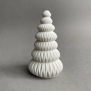 Puede incluir: Una escultura de cer&aacute;mica blanca con forma de &aacute;rbol de Navidad con una serie de niveles apilados y fruncidos.