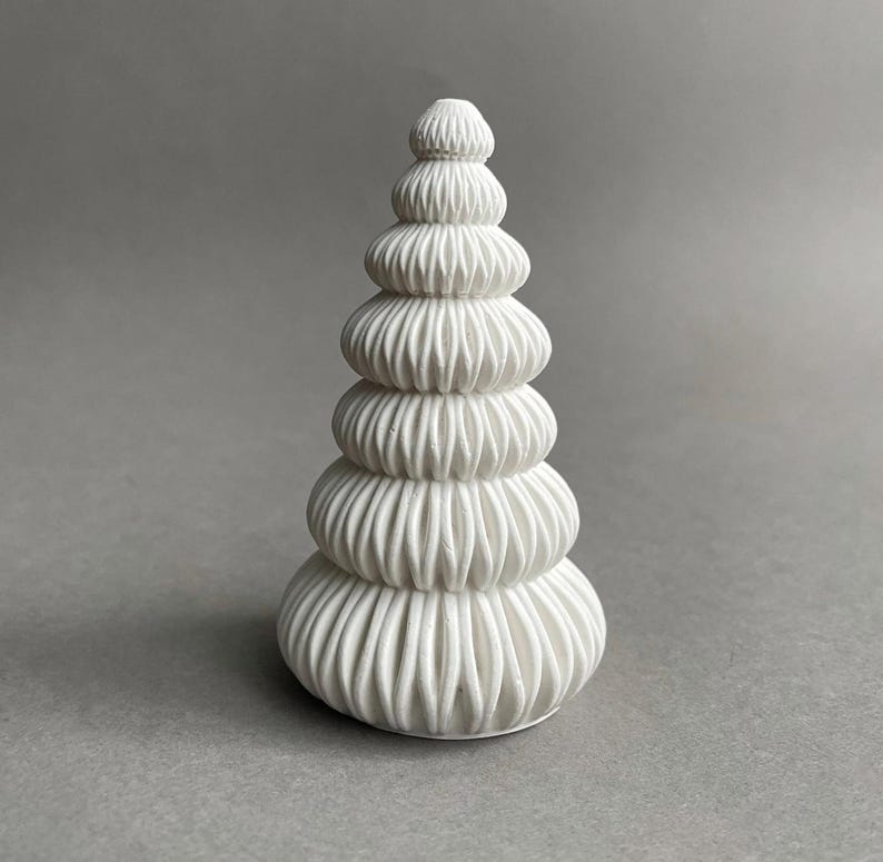 Puede incluir: Una escultura de cer&aacute;mica blanca con forma de &aacute;rbol de Navidad con una serie de niveles apilados y fruncidos.