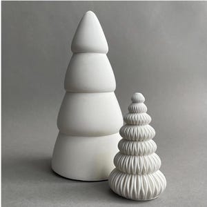 Puede incluir: Dos adornos de &aacute;rbol de Navidad de cer&aacute;mica blanca. El &aacute;rbol m&aacute;s grande es un dise&ntilde;o simple de tres niveles. El &aacute;rbol m&aacute;s peque&ntilde;o tiene un dise&ntilde;o m&aacute;s intrincado con m&uacute;ltiples niveles de volantes.