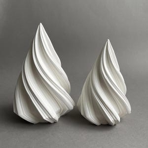 Może przedstawiać: Dwie białe ceramiczne rzeźby w kształcie stylizowanych, abstrakcyjnych drzew. Rzeźby wykonane są z gładkich, wirujących linii i mają nowoczesny, minimalistyczny charakter.