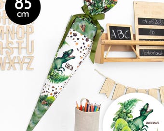 Könnte beinhalten: Ein grüner und weißer Schultüte mit einem Dinosaurier- und Blattwerkdruck. Die Tüte ist 85 cm hoch und hat den Namen "Luca" darauf gedruckt. Die Tüte ist umgeben von Schulutensilien, darunter ein Stiftehalter, Stifte und eine Tafel mit den Buchstaben "ABC" darauf.