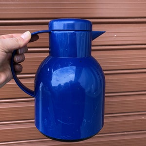 Könnte beinhalten: Eine blaue Thermokanne mit Deckel und Griff. Die Kanne ist aus Kunststoff und hat eine glänzende Oberfläche.