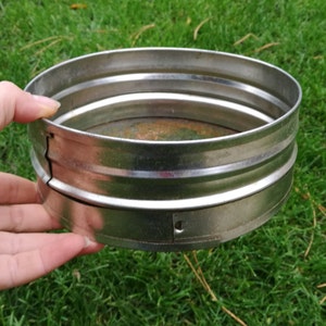 Op de afbeelding: Een zilveren metalen zeef met een gaasbodem. De zeef bestaat uit twee delen die in elkaar passen.