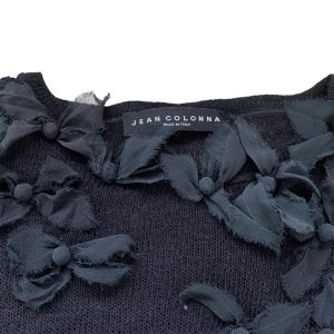 Black knitted sweater with black fabric flower embellishments. The sweater has a label that reads 'JEAN COLONNA MADE IN ITALY.'