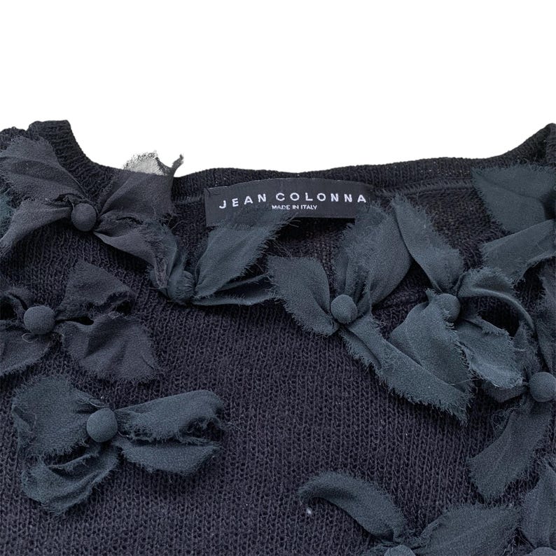 Black knitted sweater with black fabric flower embellishments. The sweater has a label that reads 'JEAN COLONNA MADE IN ITALY.'