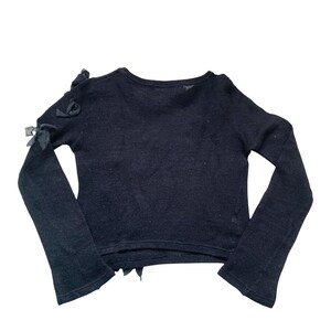 A black long-sleeved sweater with a round neckline and a slightly cropped hem. The sweater has a delicate flower details on the shoulders.