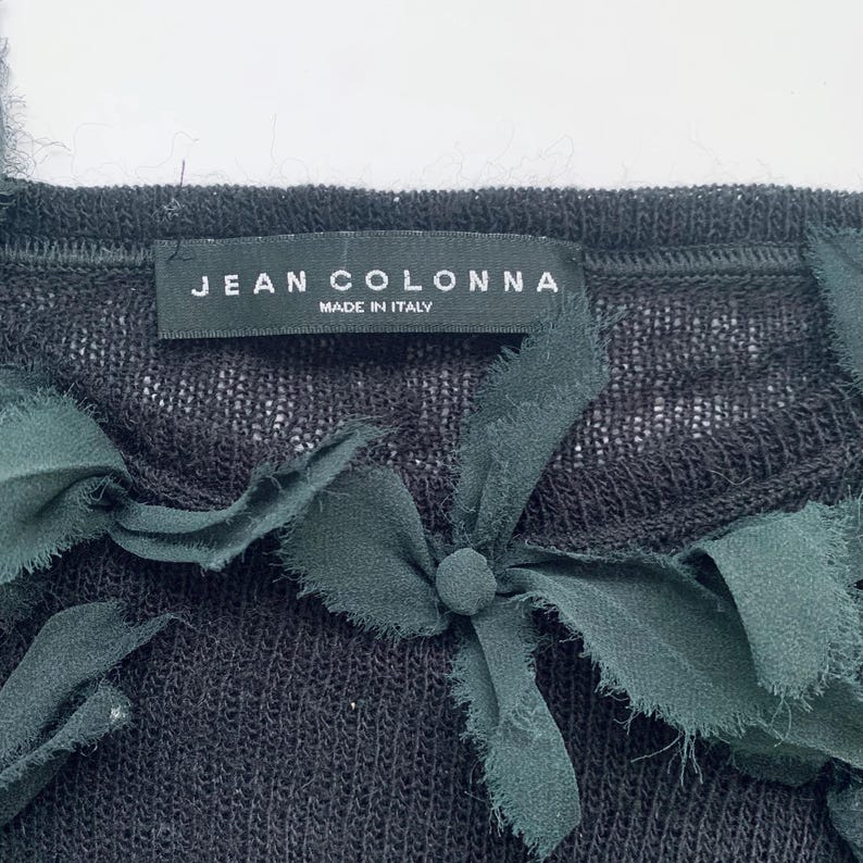 Black knit top with a fabric flowers detail. The label reads 'Jean Colonna Made in Italy.'