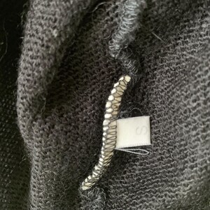 Close-up of a black sweater with a white tag sewn into the seam showing the size S.