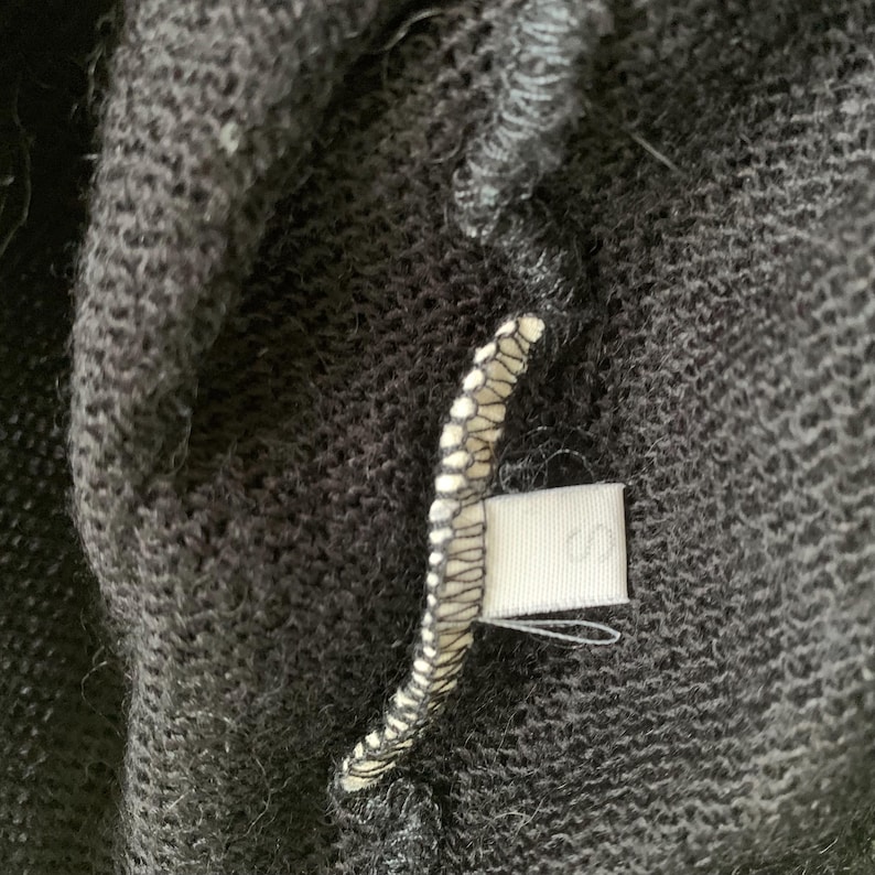 Close-up of a black sweater with a white tag sewn into the seam showing the size S.