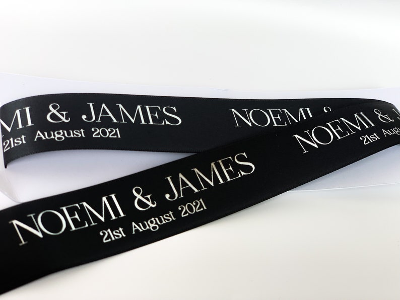 Black satin ribbon printed in white letters "Noemi & James" with date in smaller letters underneath