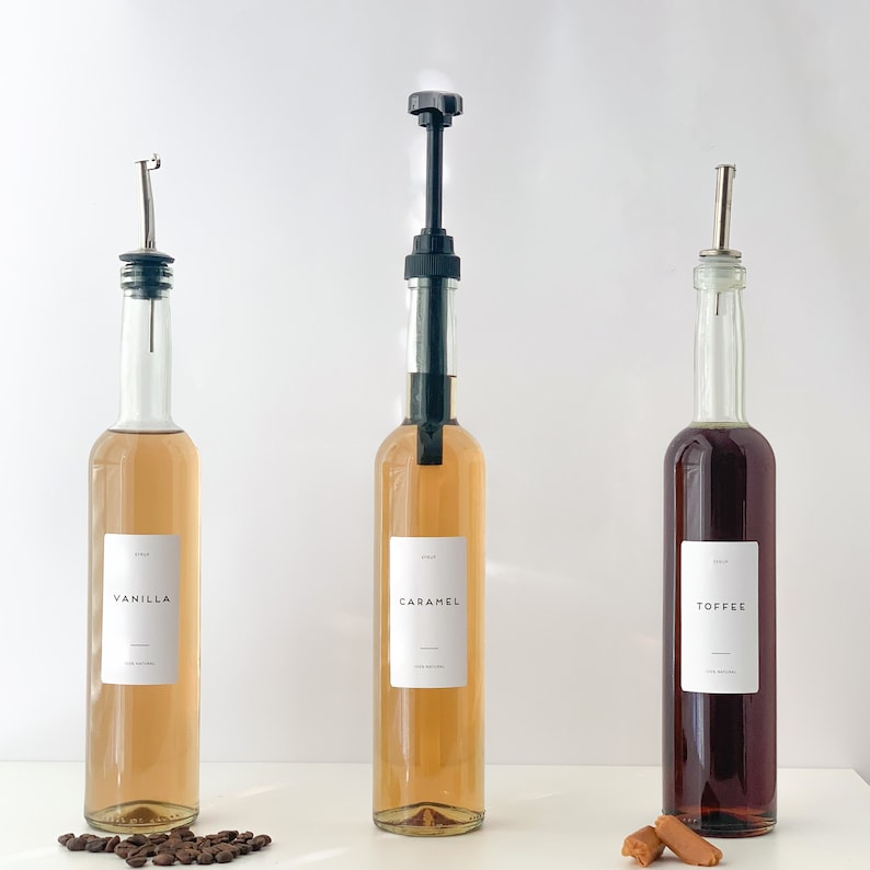 May include: Three glass bottles with pumps, filled with different colored liquids. The bottles are labeled "Vanilla", "Caramel", and "Toffee".