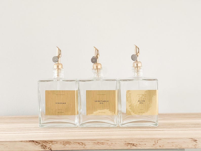 May include: Three clear glass bottles with gold spouts and labels. The labels read "Vinegar", "Vegetable Oil", and "Olive Oil".